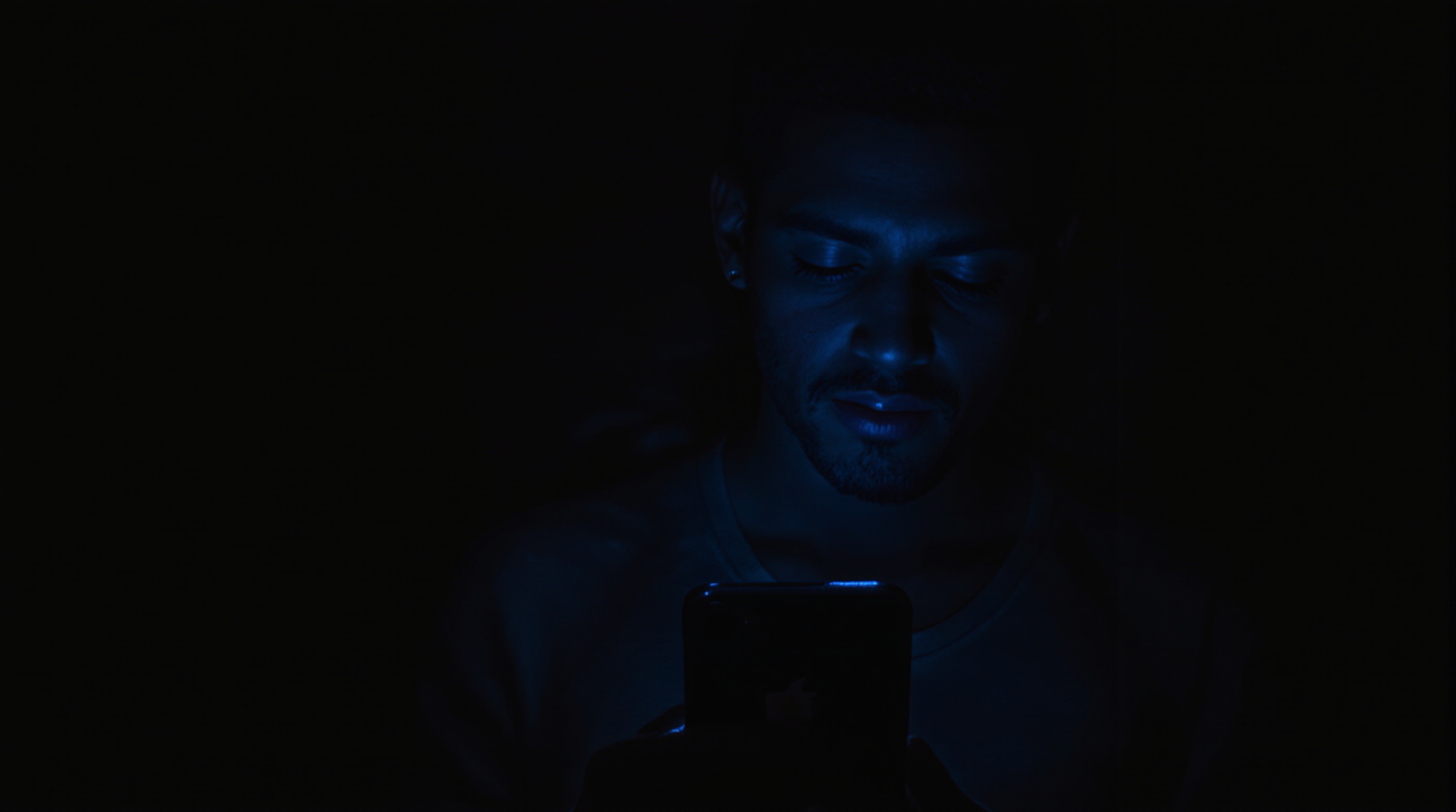Person holding an iPhone and looking at the screen with a concerned expression in a dimly lit room
