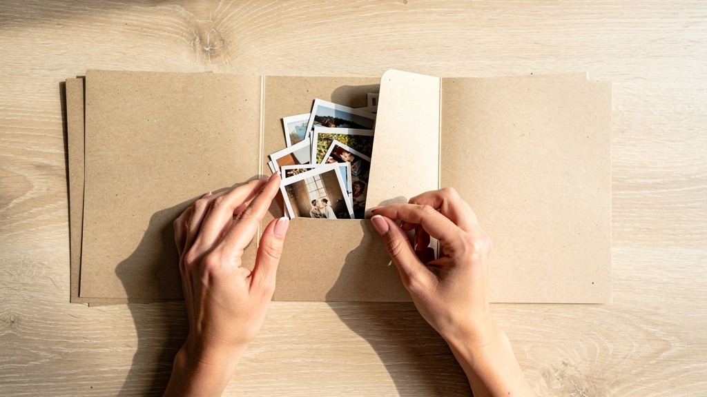 Printed photographs sorted into three neat stacks on a pale oak table beside a shoebox of loose prints