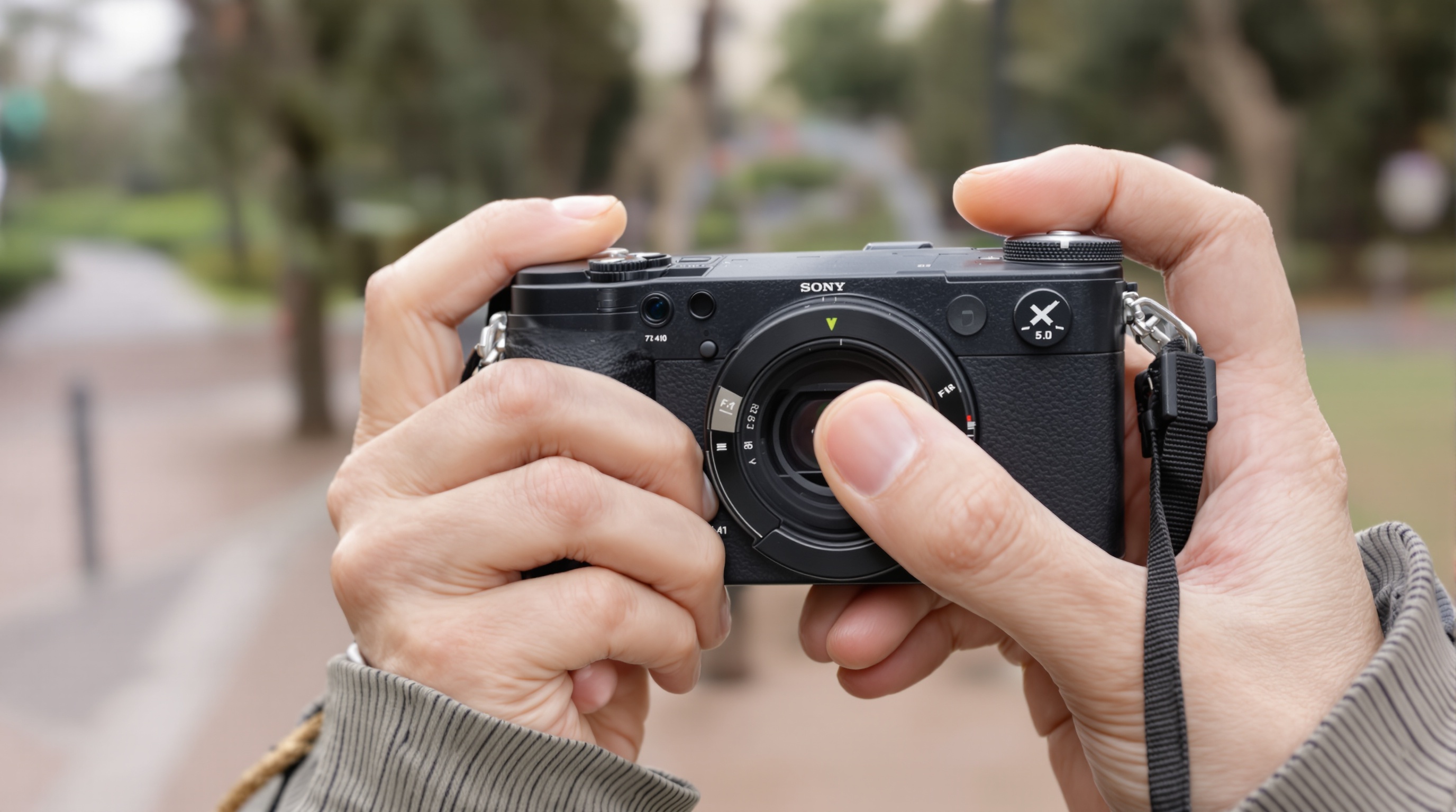 Close-up of hands holding a compact camera with manual controls visible, shallow depth of field, outdoor setting