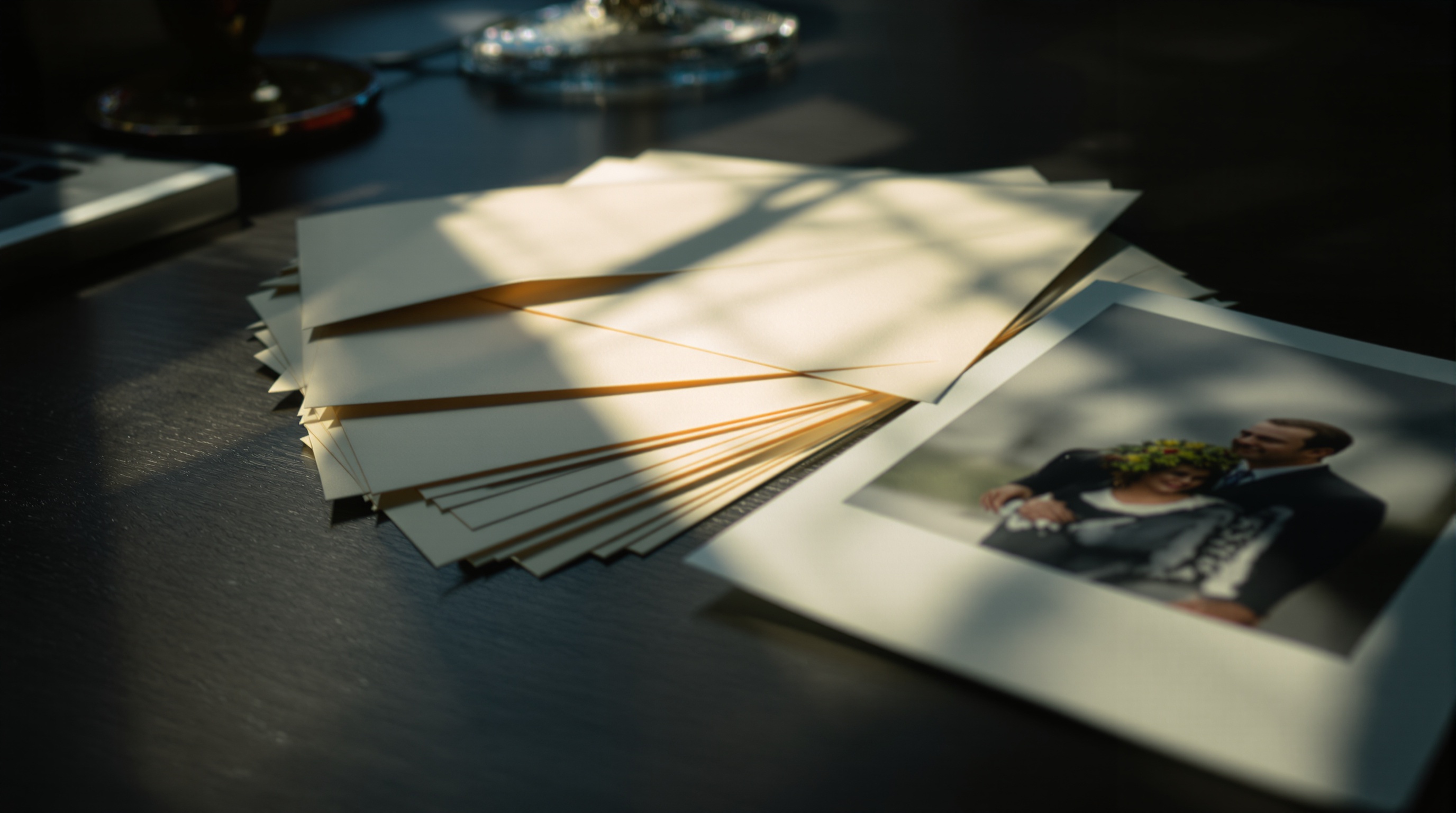 A stack of sealed envelopes next to a printed photograph on a wooden desk, warm sidelight from a window