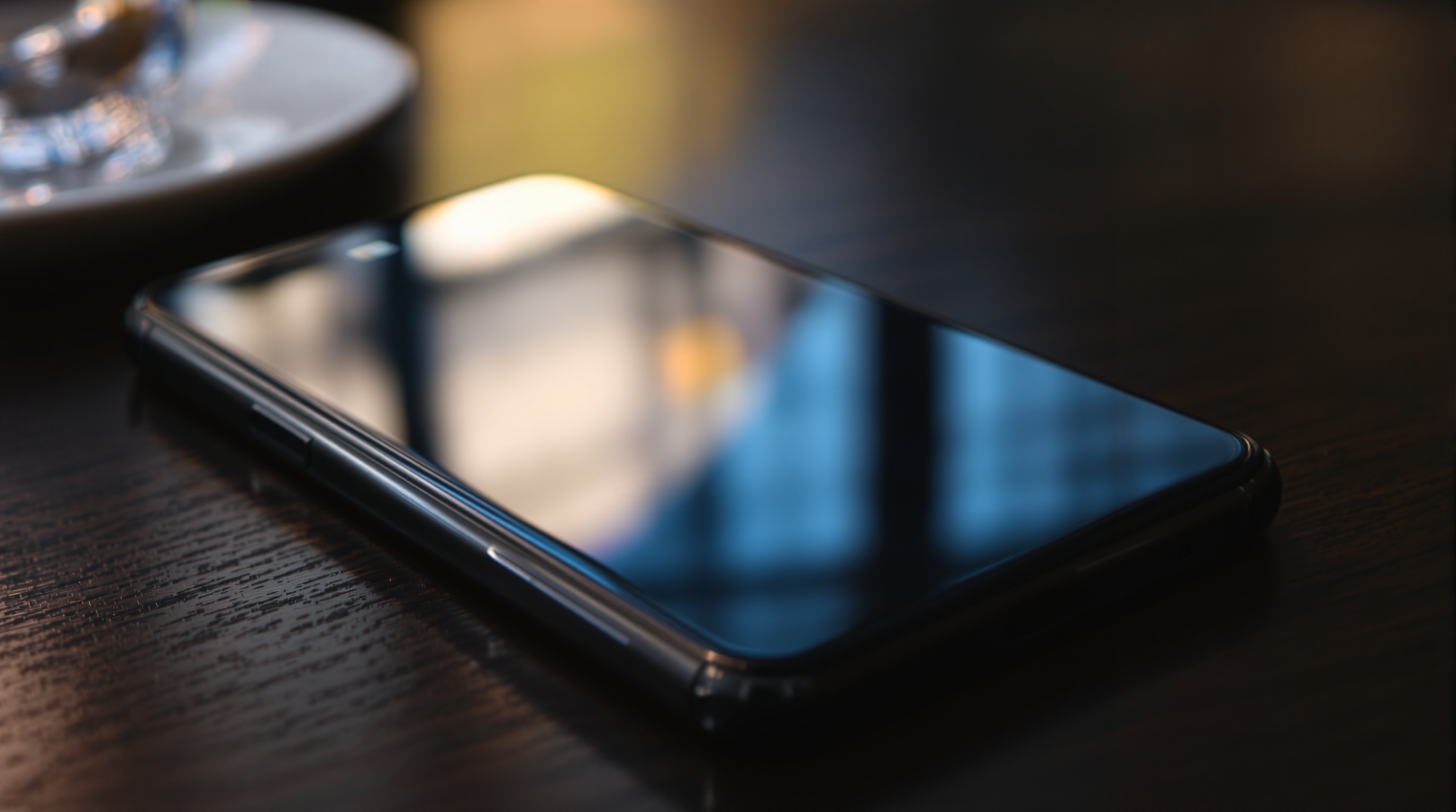 Smartphone lying face-down on a dark wooden table in a cafe, glass back reflecting ambient light, editorial still life representing the devices used to create and share AI-generated images