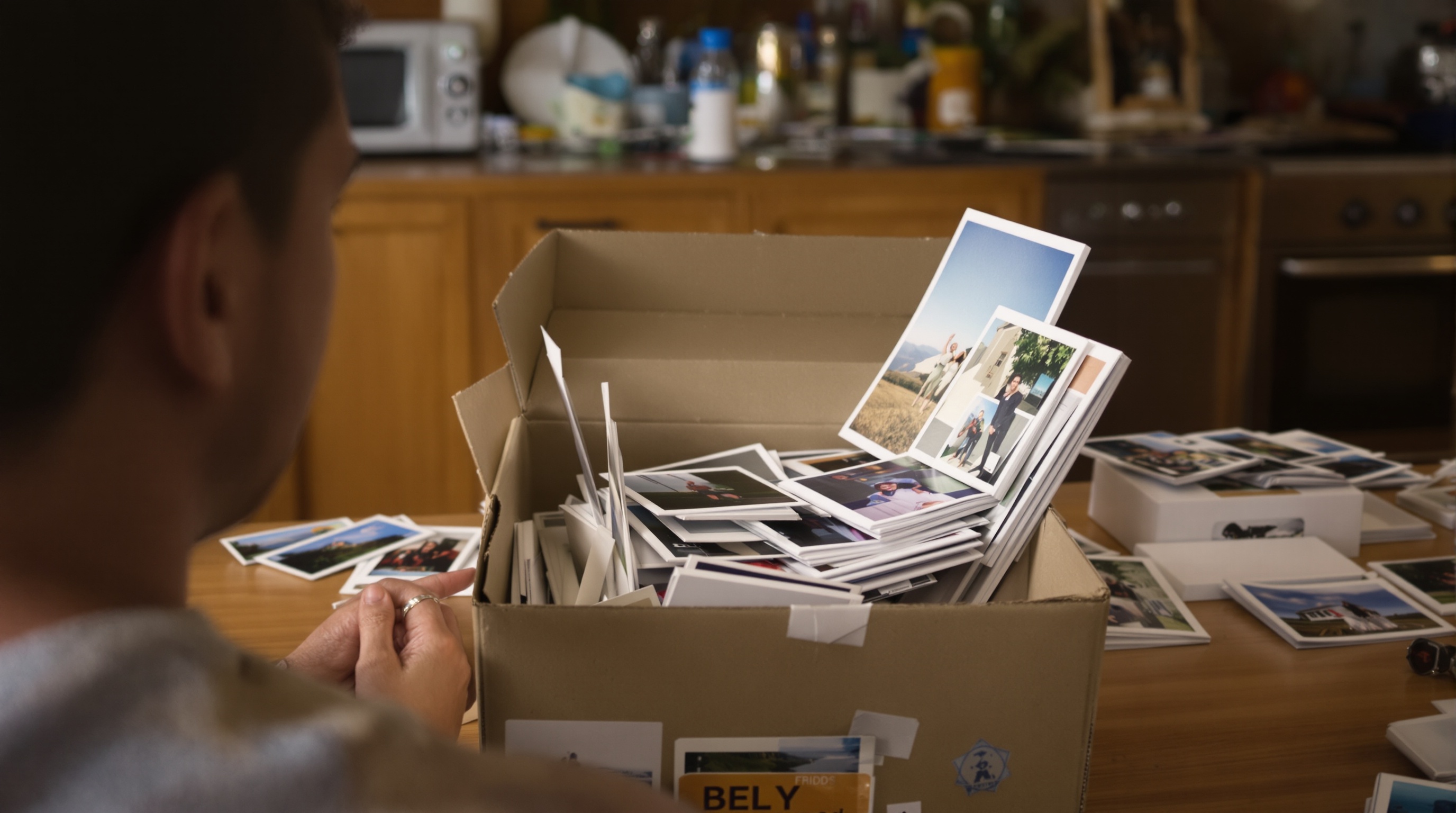 A person reviewing printed photographs at a kitchen table, natural window light from the side, shot on a 35mm lens