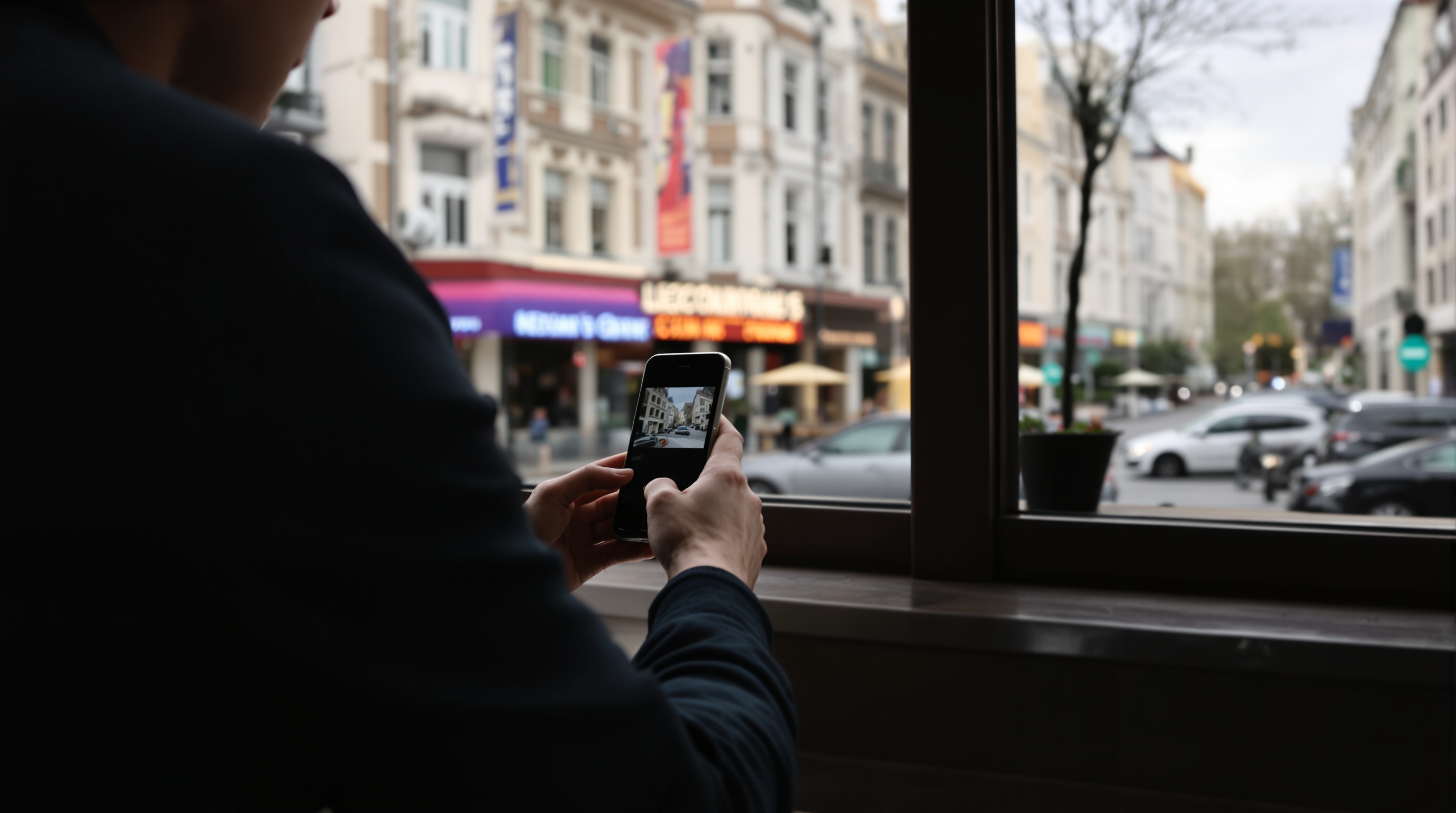 Hands holding a phone showing a photo gallery app, blurred city background visible through a cafe window