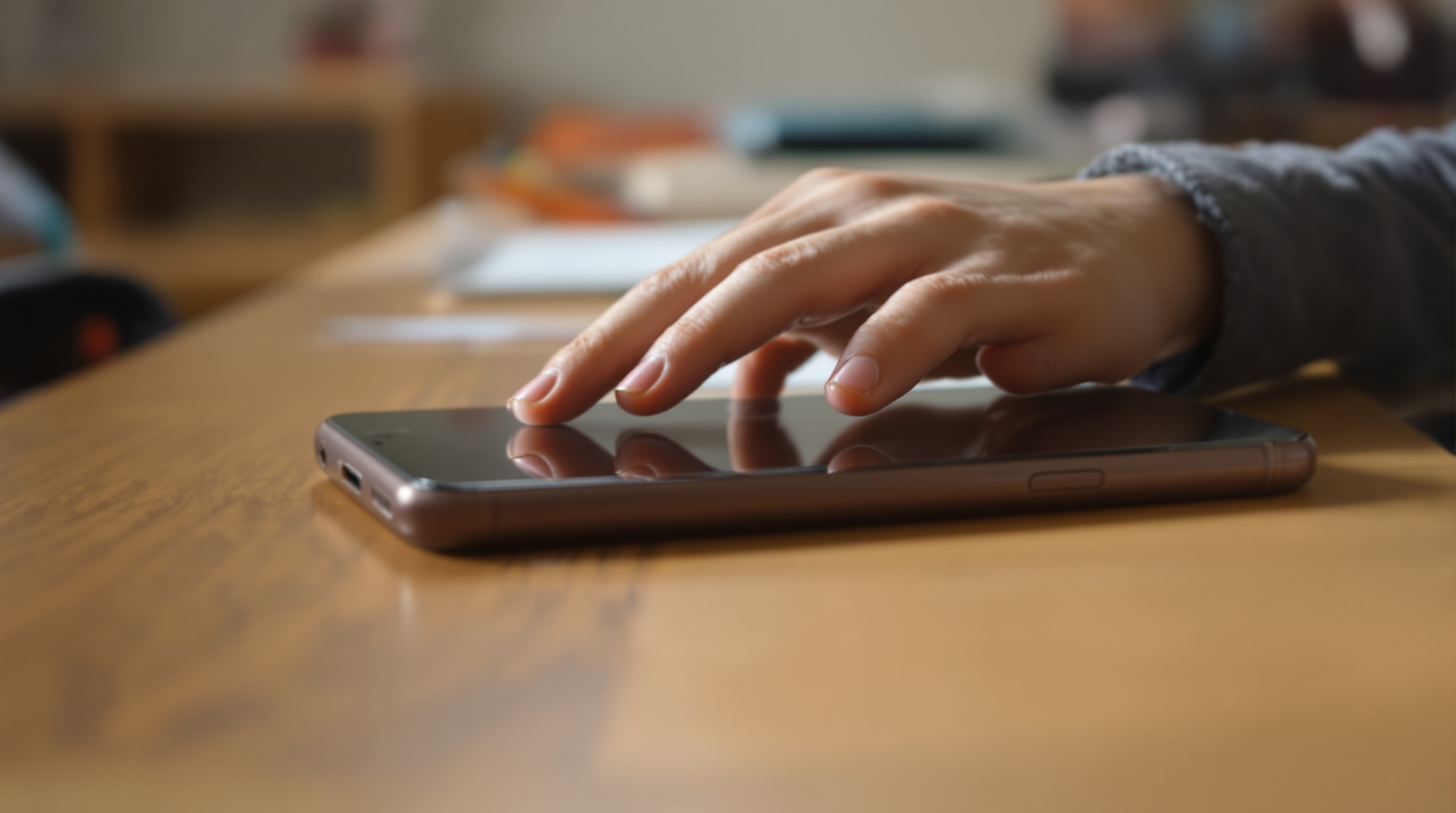 Close-up of a child placing a smartphone face-down on a wooden school desk, soft window light from the left