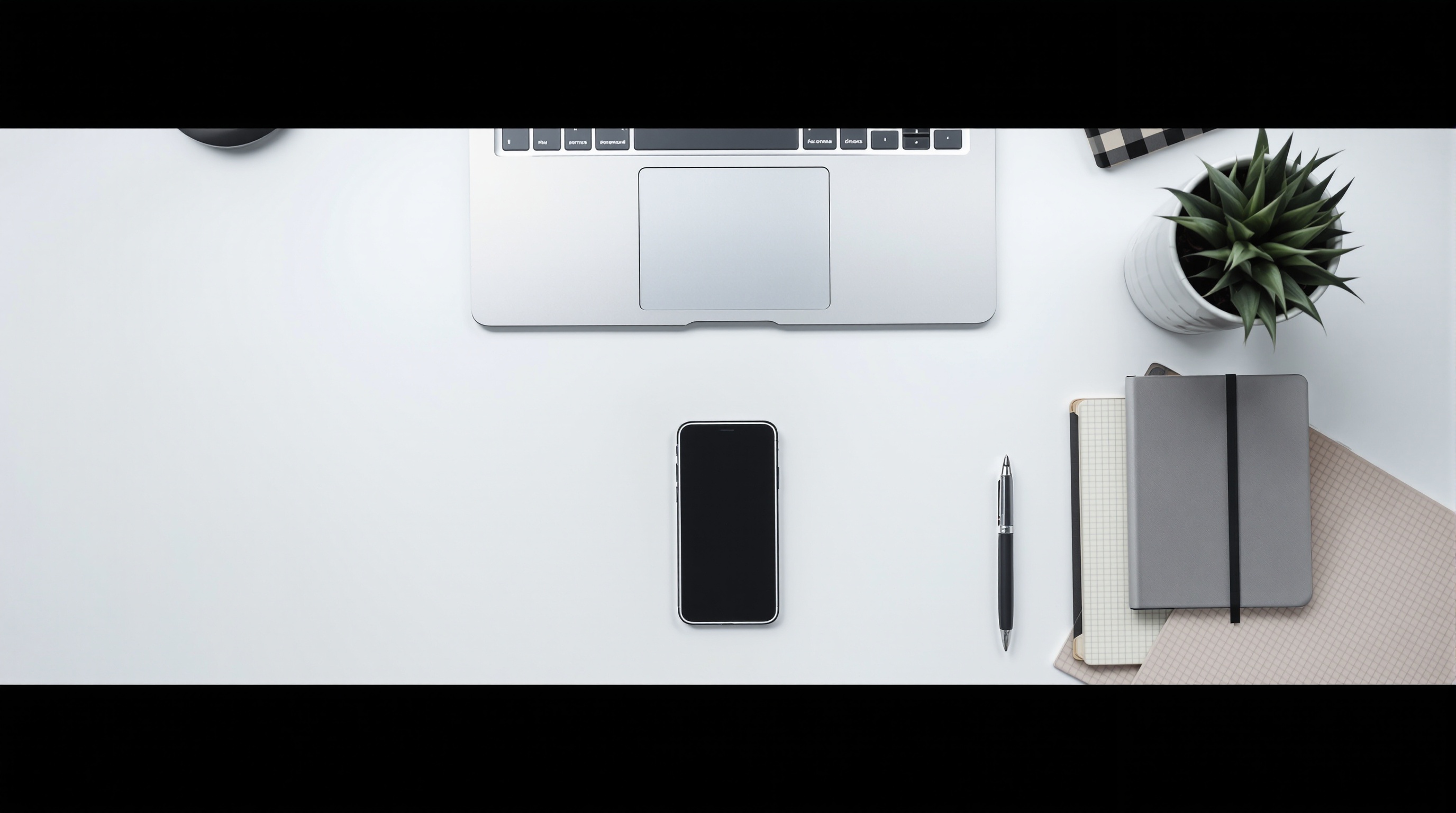 A minimalist desk setup with an iPhone, laptop, and coffee cup viewed from above
