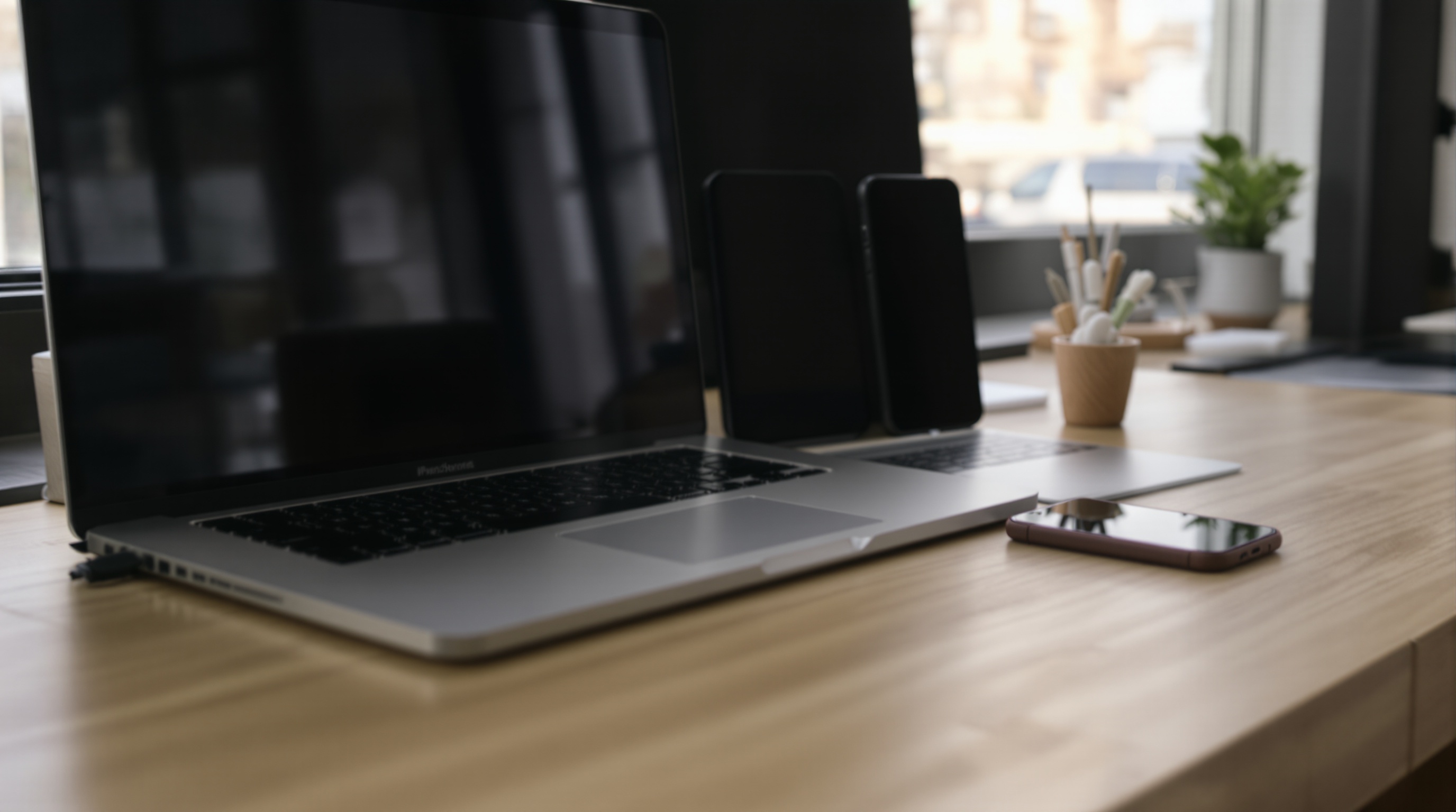 A MacBook and an iPhone side by side on a minimalist desk, both showing photo gallery interfaces, soft diffused lighting