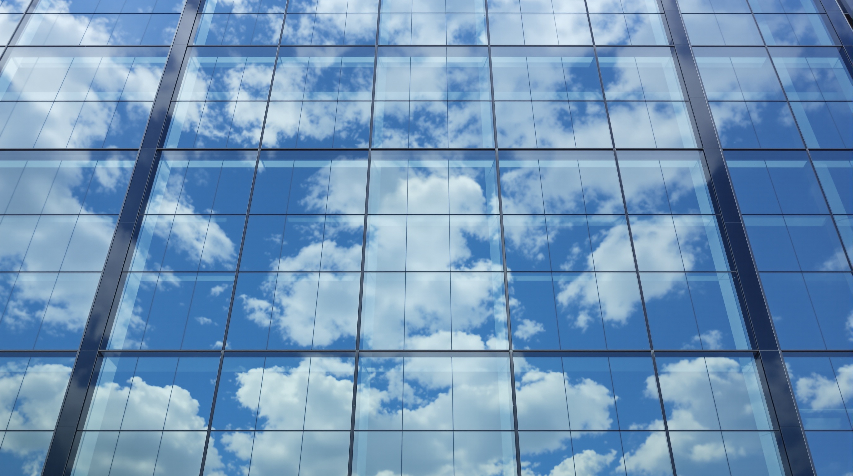 A corporate glass office building facade reflecting clouds in cool blue tones