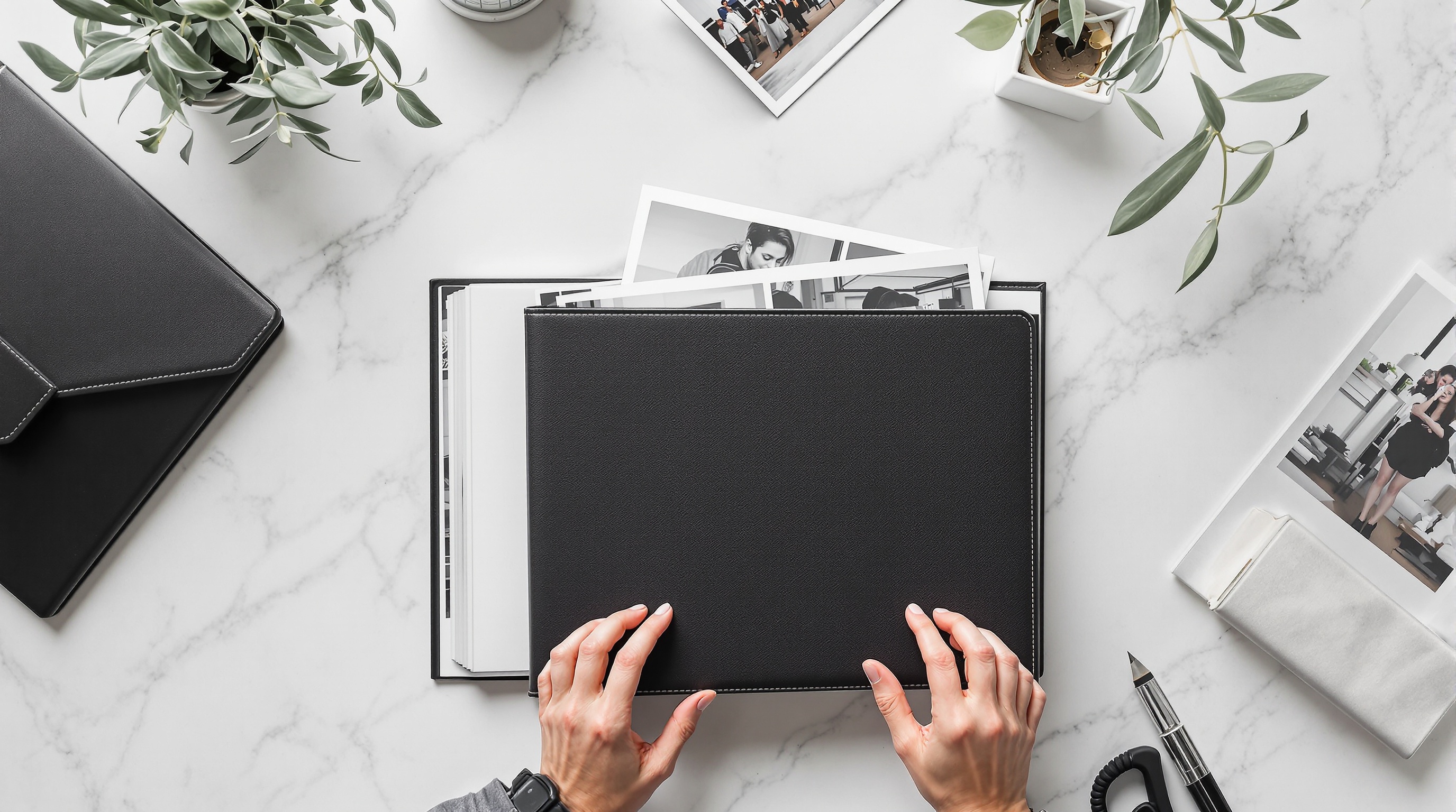 A person organizing printed photographs in a leather portfolio book, overhead flat lay with soft diffused natural light
