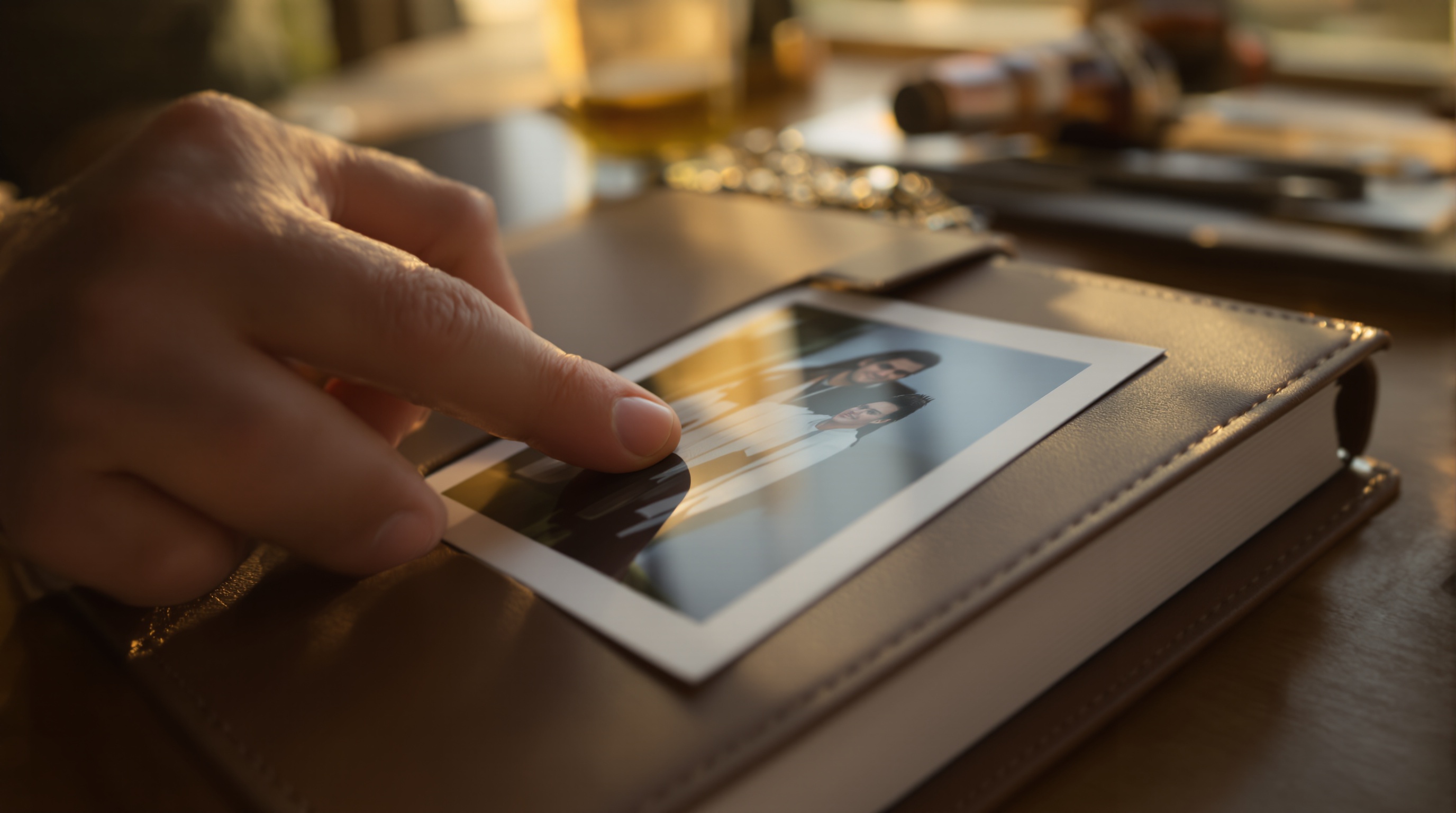 Hand carefully placing a printed photograph into a leather photo album in warm golden light