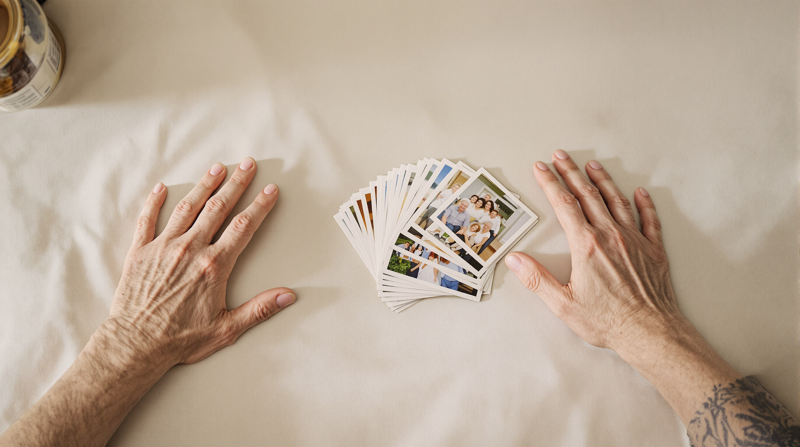 A small stack of printed portrait photographs fanned across a linen tablecloth with an older person's hand resting at the edge of the frame
