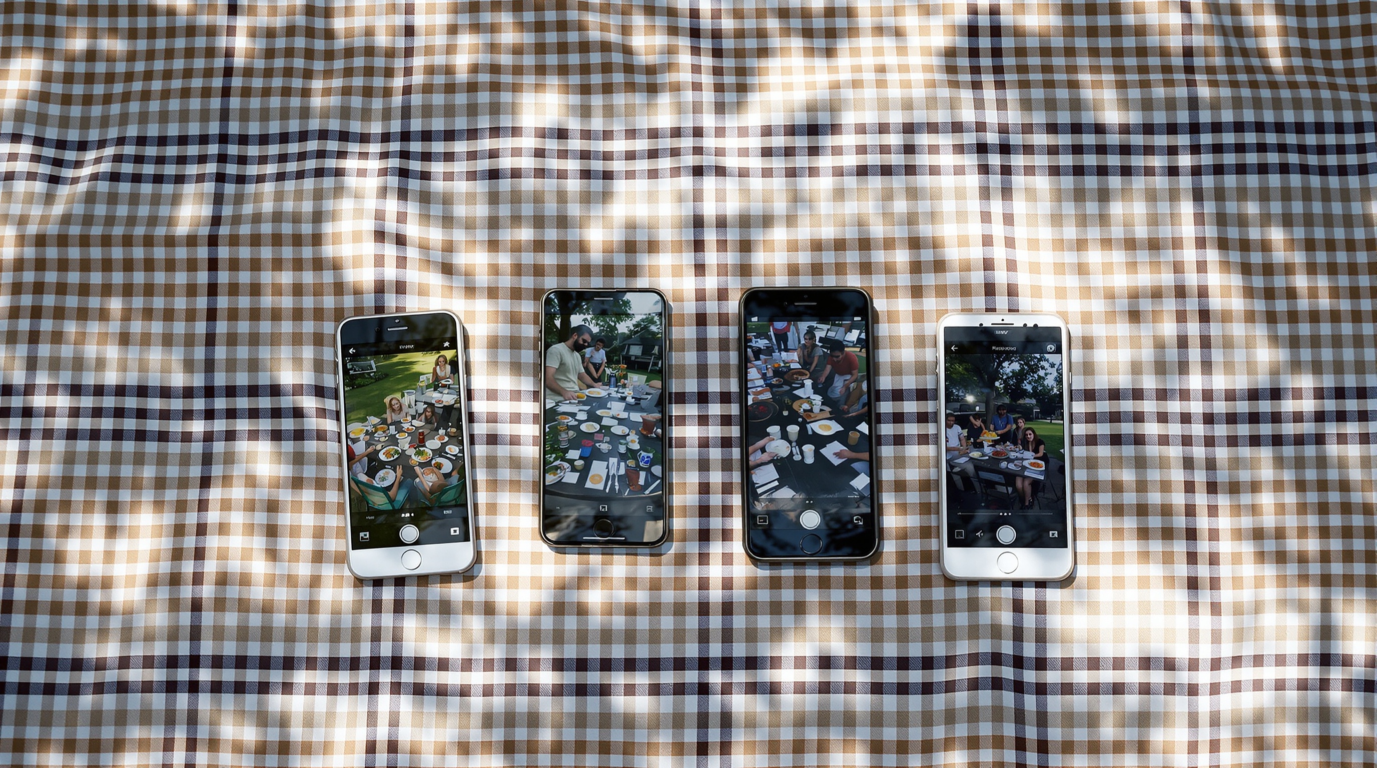 Several smartphones laid out on a blanket at a picnic, each showing different photos from the same outdoor gathering