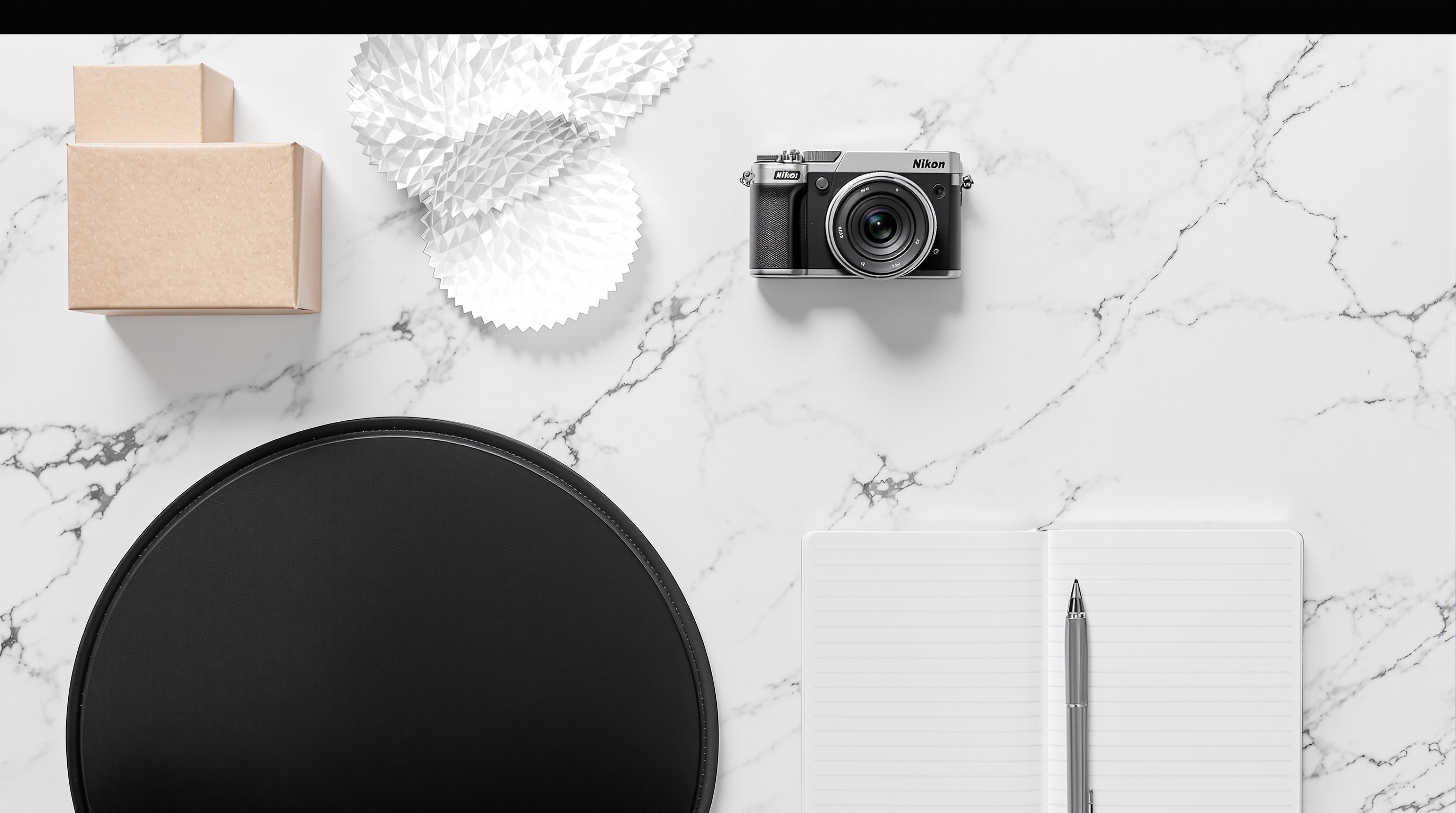 Overhead flat lay of product photography props on a white marble surface including a camera, reflector, and notebook