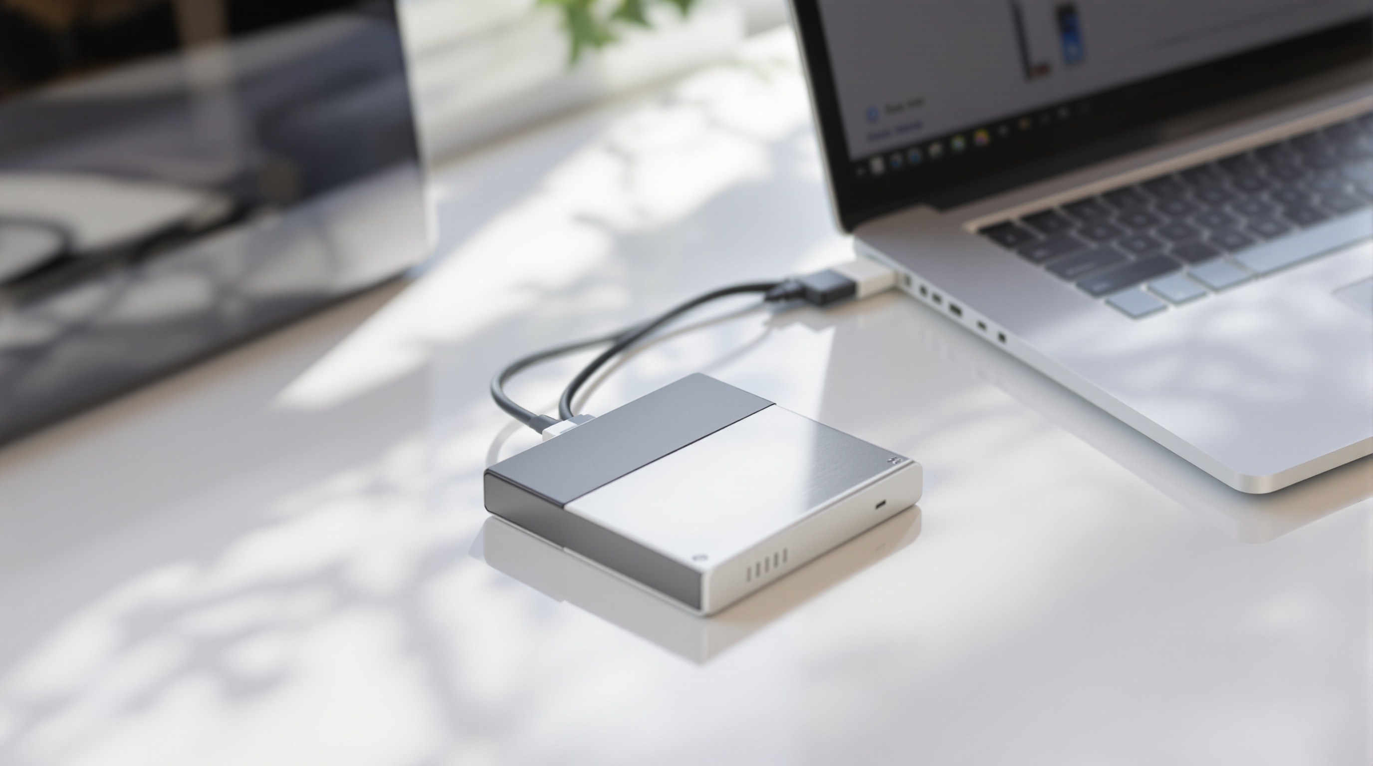 External hard drive plugged into a laptop on a clean white desk, natural daylight
