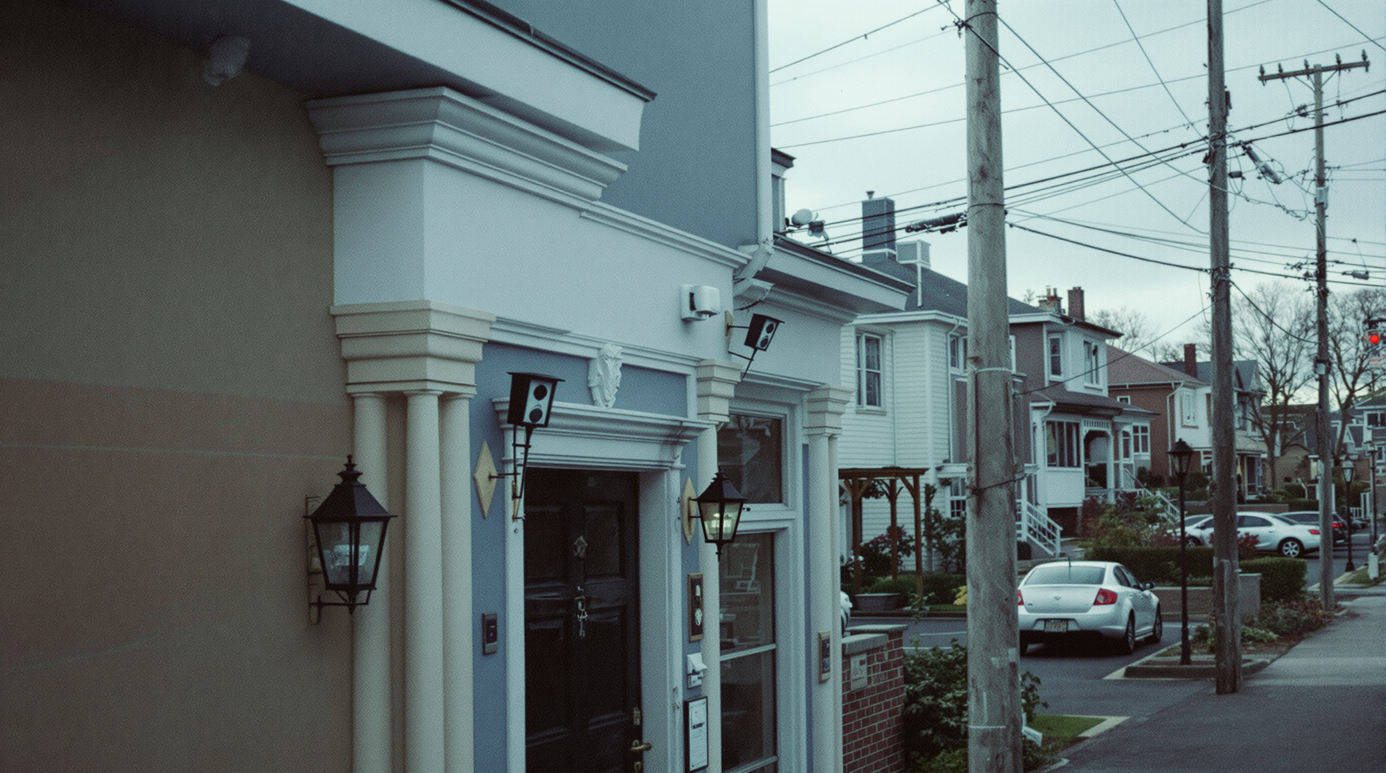 A quiet residential street with houses on both sides, porch lights visible, photographed at dusk with warm tones