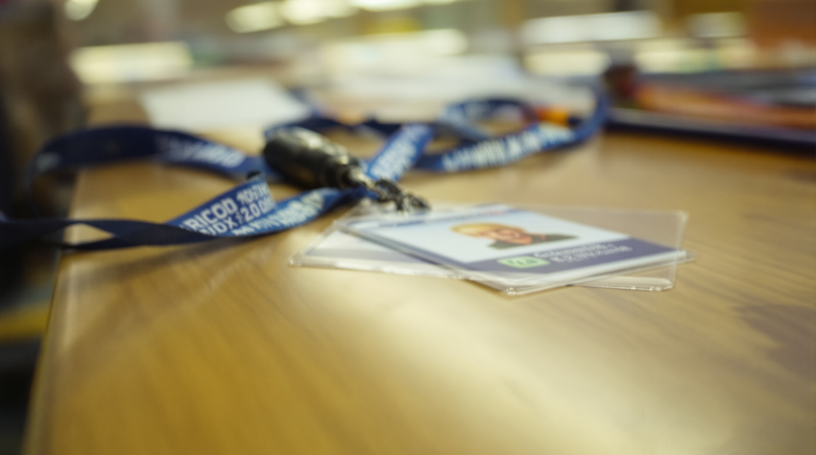 Close-up of a student ID card lanyard on a school desk next to a pencil, overhead fluorescent lighting, slight grain, representing the personal data students surrender to access school events