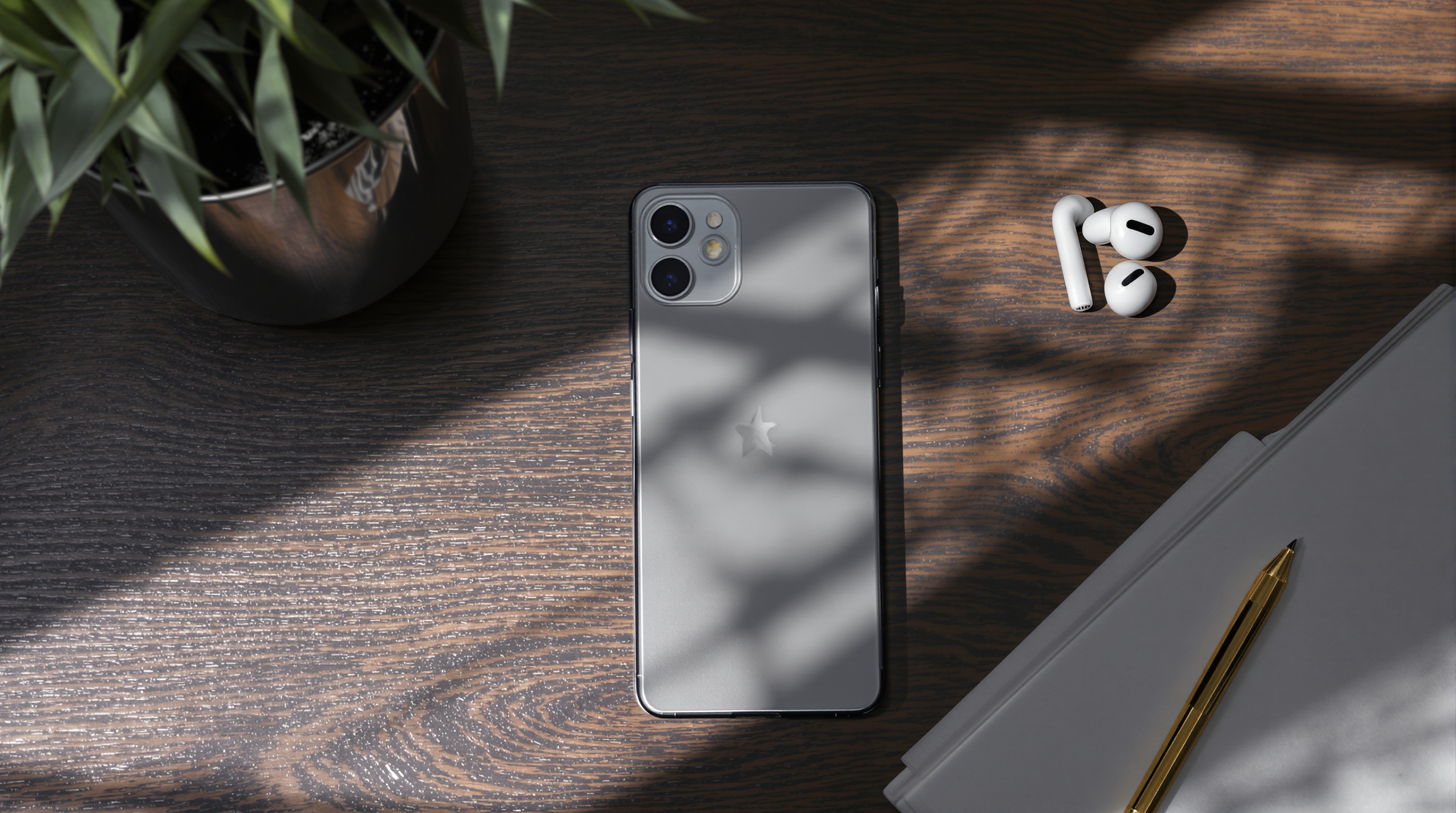 A smartphone lying on a dark wooden desk next to earbuds, soft window light illuminating the scene from the side