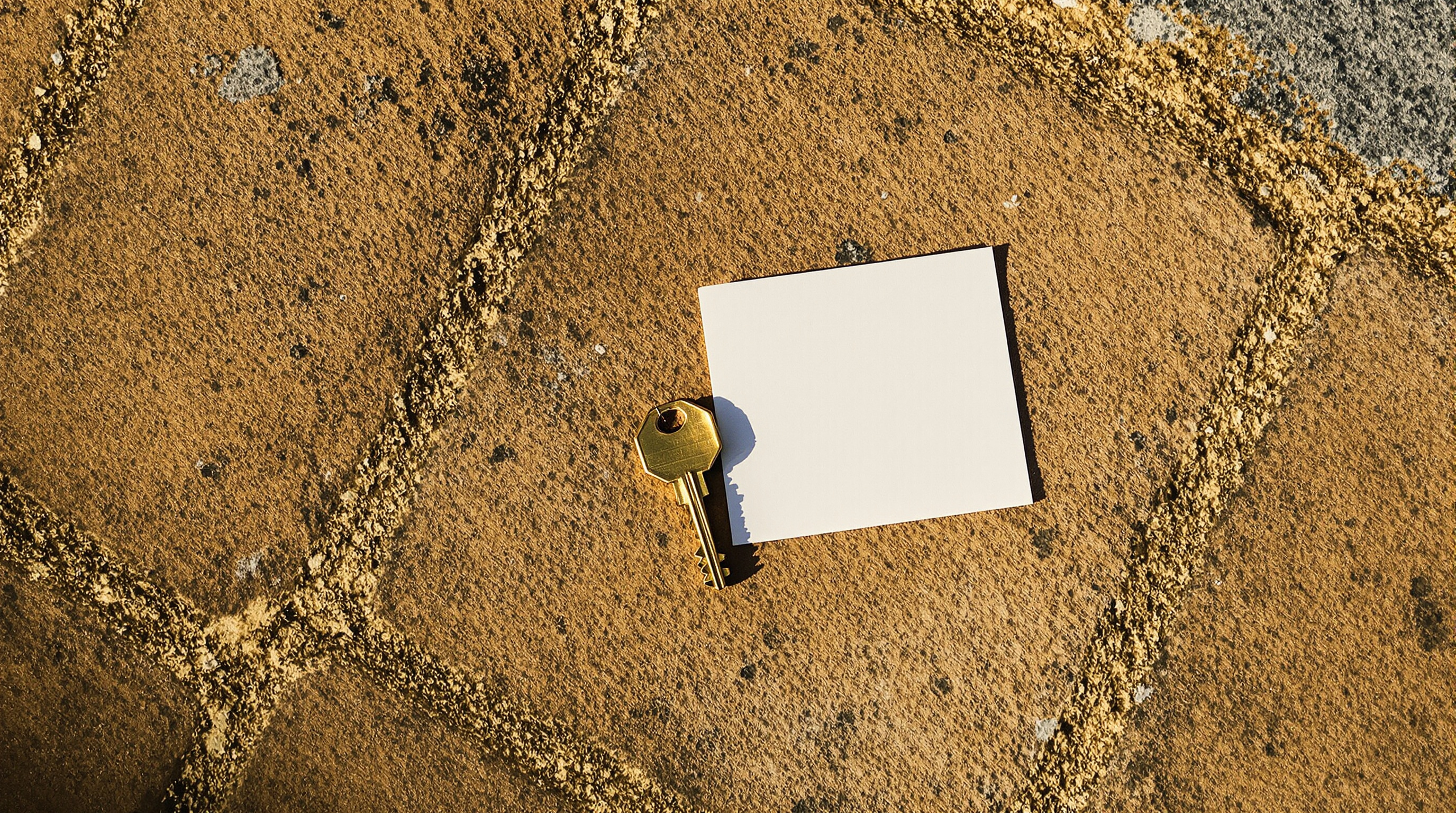 A brass door key and a folded slip of plain paper lying on a stone doorstep in low evening sun